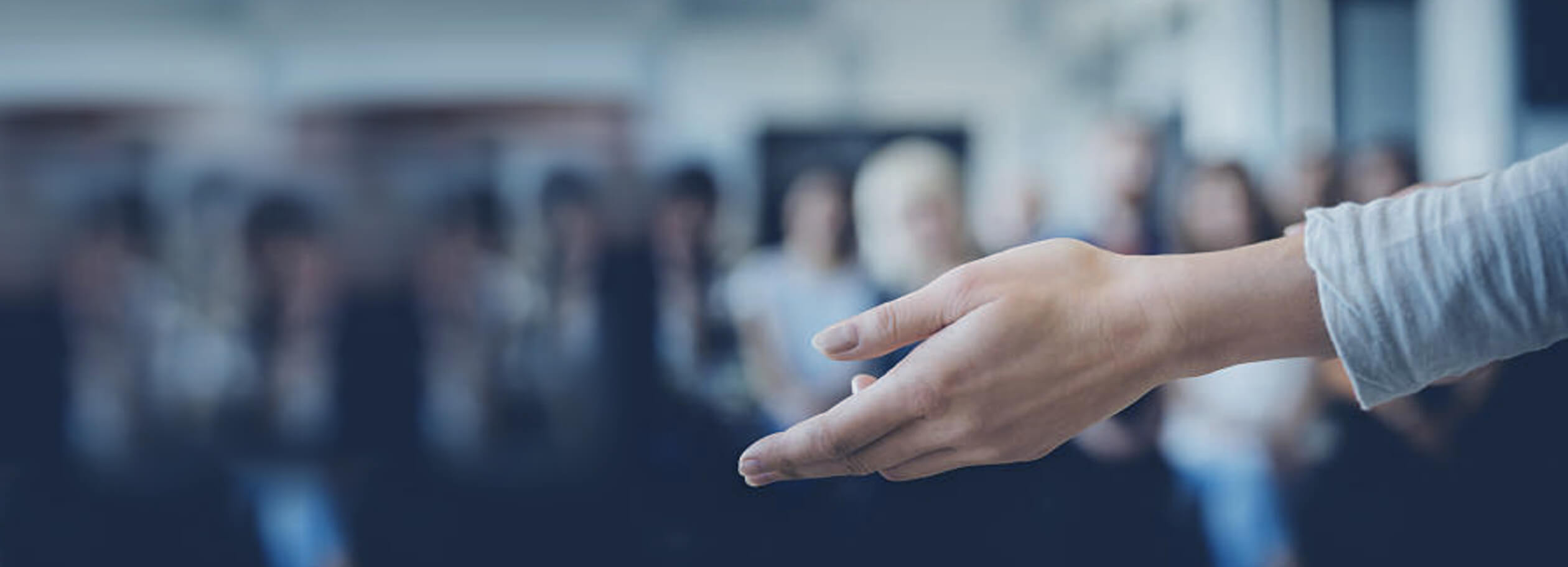 Image shows the hand of someone facing a room of people who are blurred